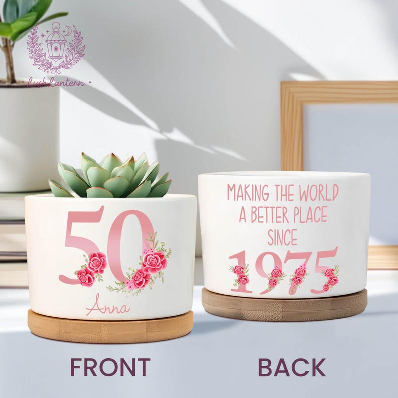 May include: Two white ceramic planters with bamboo saucers. One planter displays the number "50" in pink with floral accents and the name "Anna". The other reads "MAKING THE WORLD A BETTER PLACE SINCE 1975".