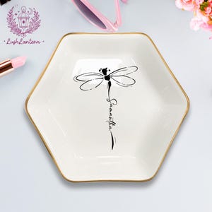 May include: A white, hexagonal trinket dish with a gold rim. A black dragonfly design is centered on the dish, with the name "Samantha" written below. The LushLantern logo is in the upper left corner.