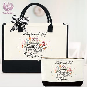 May include: Off-white tote bag and matching cosmetic bag with black accents. Both bags feature a graduation cap, diploma, and floral design with the text "Mastered It!" and "2026 Alyson". A black and white striped bow adorns the tote.
