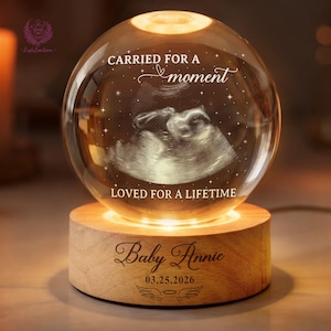 May include: A spherical crystal lamp with a wooden base. The crystal ball shows an ultrasound image and the text "CARRIED FOR A moment LOVED FOR A LIFETIME." The wooden base is engraved with the name "Baby Annie" and the date "03.25.2026".