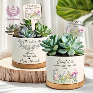 May include: Two white ceramic planters with succulents, each with a sign saying "Christal Officially Retired 2026." One planter has the text "Enjoy the next chapter" and "Happy Retirement." The planters sit on a wooden base.