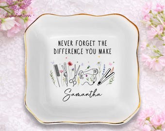 May include: White ceramic trinket dish with a gold rim. The dish features the text "NEVER FORGET THE DIFFERENCE YOU MAKE" and the name "Samantha". It also has illustrations of hairstyling tools and flowers.