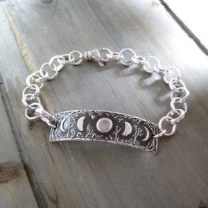 Puede incluir: Una pulsera de plata con un dije que presenta un dise&ntilde;o detallado de &aacute;rboles y fases lunares. La pulsera est&aacute; hecha de una cadena de plata con un cierre de langosta.