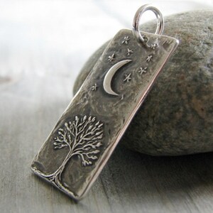 Puede incluir: Colgante de plata con una superficie texturizada que presenta un &aacute;rbol y una luna creciente con estrellas.