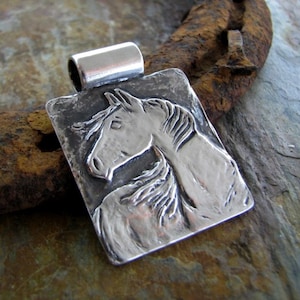 May include: A rectangular silver pendant featuring a detailed relief of a horse's head and neck. The pendant has a textured, rustic appearance with a loop at the top for a chain. The horse's mane and facial features are clearly defined.