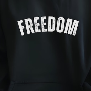 Puede incluir: Sudadera con capucha negra con la palabra "FREEDOM" impresa en letras blancas grandes y desgastadas en el pecho. La sudadera tiene una capucha con cord&oacute;n y un bolsillo de canguro. El modelo lleva vaqueros azules.