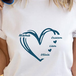 May include: White t-shirt featuring a teal heart design with the word 'Mama' on the left side of the heart. The right side of the heart has the word 'Custom' above a small heart, followed by 'Liam' and 'Olivia' below with small hearts. The shirt is plain white with rolled-up sleeves.