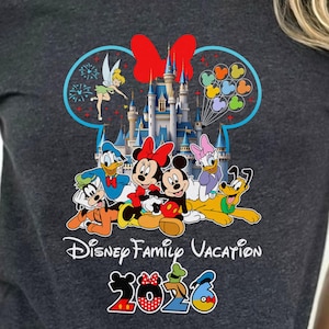 May include: Dark gray t-shirt featuring a colorful Disney Family Vacation design. The graphic includes Disney characters like Mickey and Minnie Mouse, Donald Duck, and Pluto, with a castle and the year 2026.