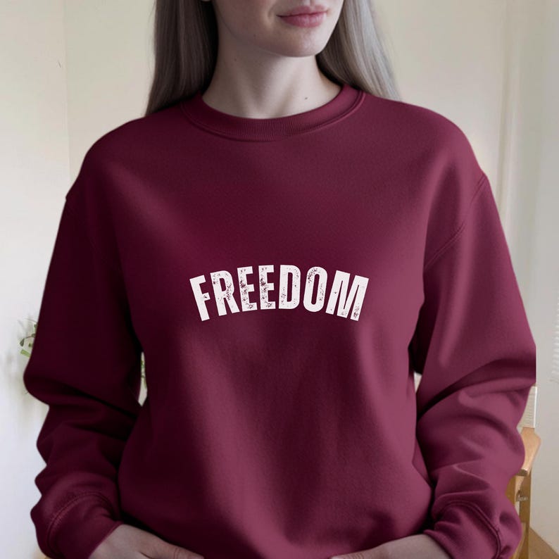 Puede incluir: Sudadera burdeos con la palabra "FREEDOM" impresa en letras blancas desgastadas en el pecho. La sudadera tiene cuello redondo y mangas largas. La tela parece ser un material suave y c&oacute;modo.