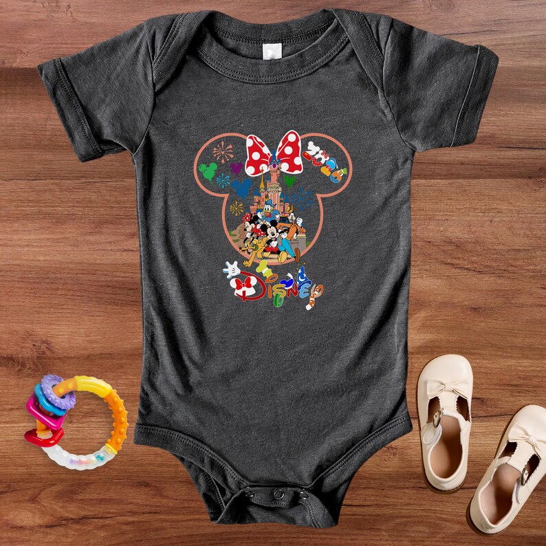 May include: Dark gray baby bodysuit featuring a colorful Disney character design. The design includes Mickey Mouse, Minnie Mouse, and other characters. A colorful baby rattle and two pairs of white baby shoes are also visible.