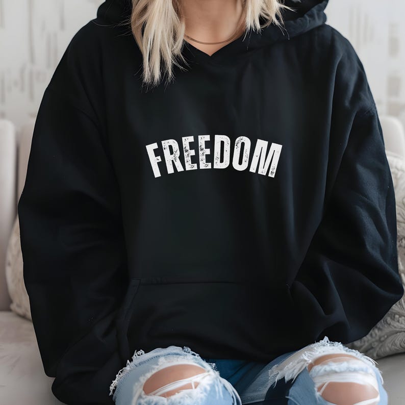 Puede incluir: Sudadera con capucha negra con la palabra "FREEDOM" impresa en letras blancas grandes y desgastadas en el pecho. La sudadera tiene una capucha con cord&oacute;n y un bolsillo de canguro. El modelo lleva vaqueros azules.