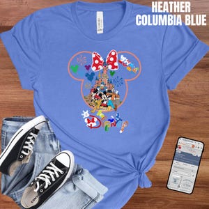 May include: Heather Columbia blue t-shirt featuring a colorful Disney graphic. The design includes Mickey and Minnie Mouse, a castle, and the word "Disney". The shirt is paired with black sneakers and blue jeans.