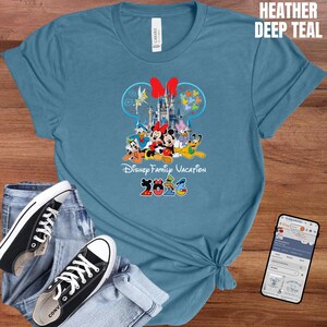 May include: A heather deep teal t-shirt featuring a Disney Family Vacation design with Mickey and Minnie Mouse, Donald Duck, and other characters. The design includes a castle and the year 2023.