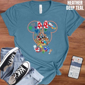 May include: Heather deep teal t-shirt featuring a Minnie Mouse design with a red and white polka dot bow, a castle, and various Disney characters. The shirt is paired with blue jeans and black Converse sneakers.