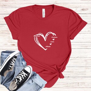 May include: Red t-shirt with a white heart design. The heart contains the words "Mama", "Custom", "Liam", and "Olivia". Black and white sneakers and blue jeans are in the foreground.