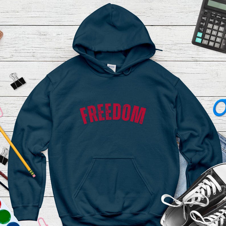 Puede incluir: Una sudadera con capucha azul marino con la palabra "FREEDOM" impresa en rojo en el pecho. La sudadera tiene un bolsillo delantero y una capucha con cord&oacute;n. La prenda est&aacute; hecha de un material suave.