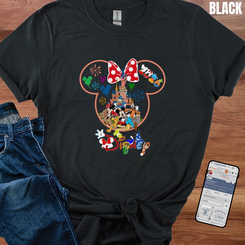 May include: Black t-shirt featuring a colorful Disney design. The design includes a Minnie Mouse bow, Disney characters, and the word "Disney" in a playful font. The shirt is paired with blue jeans.