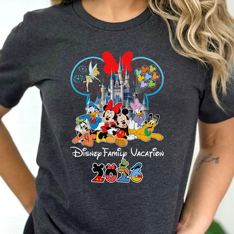 May include: Dark gray t-shirt featuring a colorful Disney Family Vacation design. The graphic includes Disney characters like Mickey and Minnie Mouse, Donald Duck, and Pluto, with a castle and the year 2026.