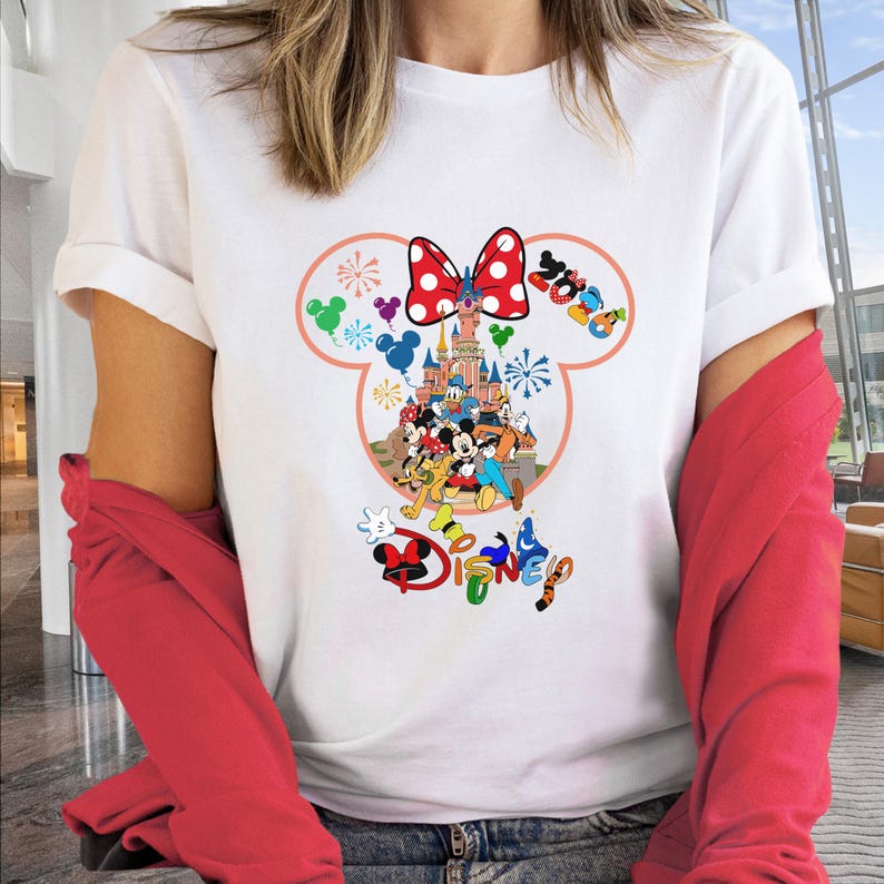 May include: White t-shirt featuring a colorful Disney graphic. The design includes a red polka-dot bow, a castle, and various Disney characters. The word "Disney" is also displayed in multiple colors.