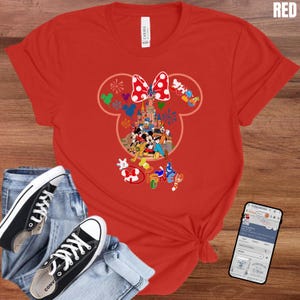 May include: Red t-shirt featuring a Mickey Mouse head design with a castle, characters, and the word "Disney". The design includes a red and white polka dot bow. Black sneakers and blue jeans are also in the image.