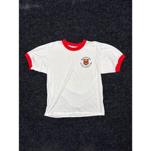 May include: A white short-sleeve ringer t-shirt with red trim on the crew neckline and sleeve cuffs. The front features a circular graphic logo on the left chest that reads Westover Air Force Base, Ma. with a central shield emblem in red and yellow.
