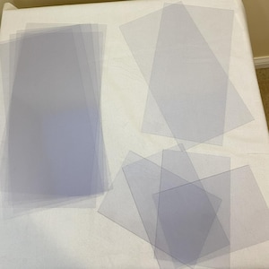 以下が含まれることがあります： さまざまなサイズの透明なプラスチックシートのスタック。シートは半透明で、わずかに光沢があります。