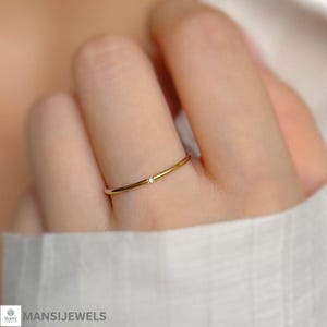 Op de afbeelding: Een delicate gouden ring met een kleine, heldere edelsteen. De ring heeft een minimalistisch ontwerp en wordt op een vinger getoond. De achtergrond is wazig, waardoor de focus op de sieraden ligt.