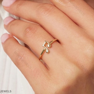 May include: A gold-colored ring featuring a musical note design. The ring is a delicate piece of jewelry, with the note symbol as the focal point. The ring is worn on a finger, showcasing its elegant and simple design.