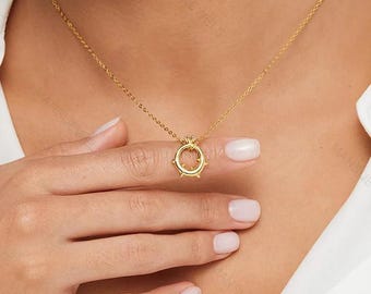 May include: A gold-colored necklace with a circular pendant featuring small spikes. The necklace is worn on a person's neck, and the pendant is centered. The background is a white shirt.