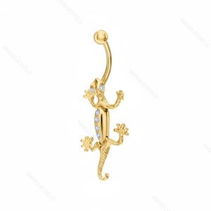 May include: A gold-colored belly button ring in the shape of a lizard. The lizard has a curved barbell design with a small ball at the top and a lizard-shaped charm. The charm is adorned with small, clear gemstones. The lizard's body is detailed with tiny feet and a curled tail.