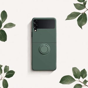 May include: A dark green phone case with a ring holder, designed for a folding phone. The case has a solid colour with a matte finish. The phone case is shown open and closed, with the camera visible.