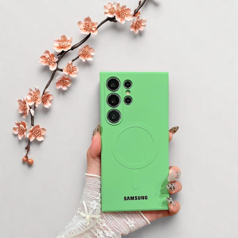 Peut inclure: Coque de t&eacute;l&eacute;phone vert vif avec un design circulaire et le mot "SAMSUNG" en bas. L'&eacute;tui pr&eacute;sente une d&eacute;coupe pour l'appareil photo avec plusieurs objectifs. Une branche florale d&eacute;corative avec des fleurs roses en arri&egrave;re-plan.