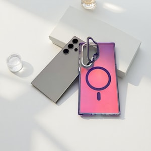May include: A silver smartphone and a clear phone case with a pink and purple gradient design. The case has a dark purple border and a circular design on the back. A small glass container is also visible.