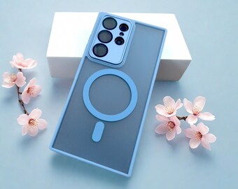 May include: A blue phone case with a light blue border and a circular design. The case has a camera cutout and a magnetic ring. Pink flowers are arranged around the case on a light blue surface.
