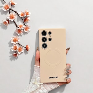 Peut inclure: Coque de t&eacute;l&eacute;phone beige clair avec un design circulaire et le logo Samsung. L'&eacute;tui pr&eacute;sente plusieurs d&eacute;coupes pour l'appareil photo et une finition lisse. Une branche de fleurs blanches et orange est en arri&egrave;re-plan.