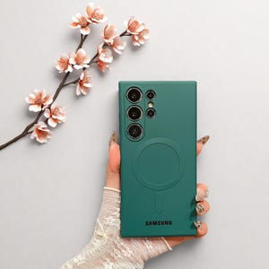 Peut inclure: Une coque de t&eacute;l&eacute;phone vert d'eau avec un design circulaire et le logo Samsung. L'&eacute;tui comporte plusieurs d&eacute;coupes pour l'appareil photo et un anneau magn&eacute;tique. Une branche avec des fleurs roses est en arri&egrave;re-plan.
