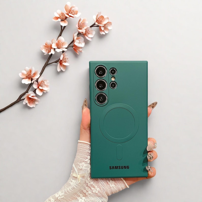 Peut inclure: Une coque de t&eacute;l&eacute;phone vert d'eau avec un design circulaire et le logo Samsung. L'&eacute;tui comporte plusieurs d&eacute;coupes pour l'appareil photo et un anneau magn&eacute;tique. Une branche avec des fleurs roses est en arri&egrave;re-plan.