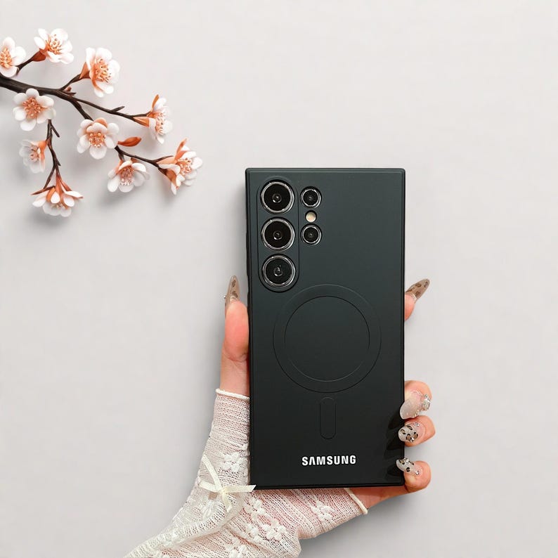 Peut inclure: Coque de t&eacute;l&eacute;phone noire avec un design circulaire et le logo Samsung. L'&eacute;tui comporte plusieurs d&eacute;coupes pour l'appareil photo. Une branche de fleurs blanches et roses se trouve dans le coin sup&eacute;rieur gauche.