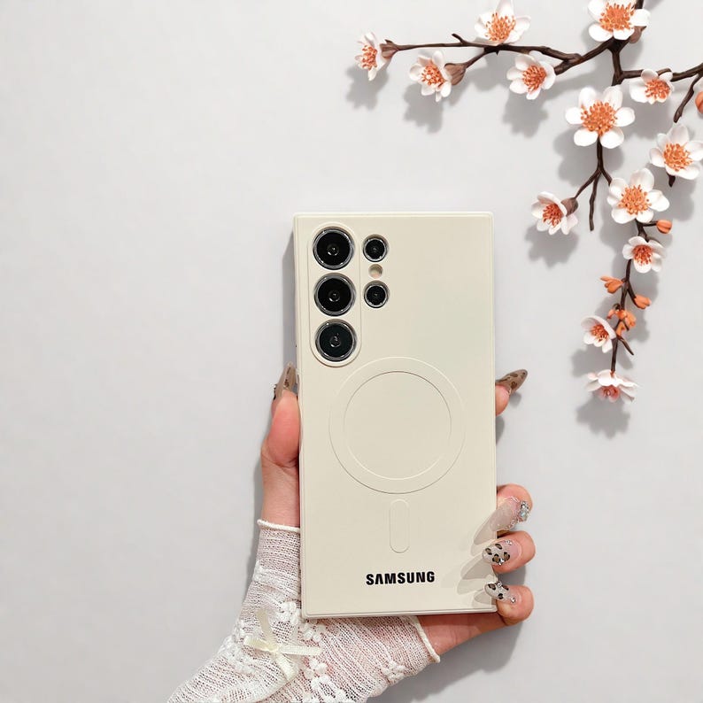 Peut inclure: Coque de t&eacute;l&eacute;phone Samsung cr&egrave;me avec un design circulaire et le nom de la marque en bas. L'&eacute;tui comporte plusieurs d&eacute;coupes pour l'appareil photo. Le fond pr&eacute;sente une surface blanche et une branche avec des fleurs blanches et orange.