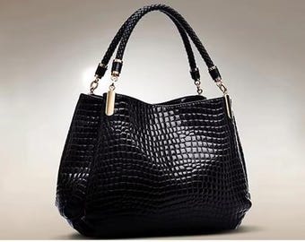 May include: A black handbag with a textured, crocodile-effect pattern. The bag has a plaited handle and gold-coloured accents. The bag is a medium size and appears to be made of leather.