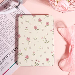 Op de afbeelding: Een crèmekleurige tablethoes met een bloemenpatroon van roze bloemen en groene bladeren. Het ontwerp herhaalt zich over het hele oppervlak. De hoes is rechthoekig met afgeronde hoeken, wat een zachte, vrouwelijke uitstraling creëert.