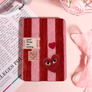 May include: A red and pink striped notebook with patches of hearts and the text "good things are coming." The notebook has a vintage aesthetic with a heart-shaped stamp and a ticket-style label.