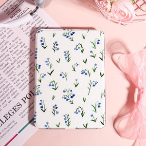 May include: A white rectangular case with a floral pattern of blue bellflowers and green leaves. The case has a smooth surface and a rounded edge. The design is a repeating pattern of the flowers and leaves.