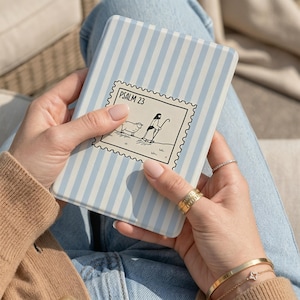 May include: A rectangular e-reader cover featuring a light blue and white vertical striped pattern. Centered on the cover is a black and white graphic resembling a postage stamp with the text PSALM 23 and an illustration of a shepherd and sheep.