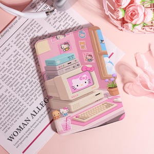 Può includere: Custodia per laptop rosa a tema Hello Kitty con un design di computer retrò. La custodia include una tastiera, un monitor e adesivi decorativi. Il testo "KELO" è visibile sul monitor. La custodia ha una combinazione di colori rosa e bianco.