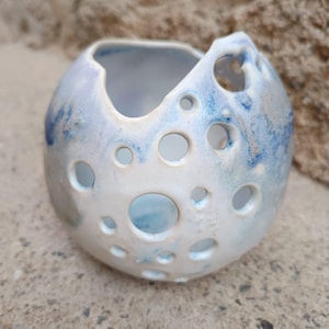 May include: A white ceramic bowl with a blue and white glaze. The bowl has a unique design with many holes throughout the surface.
