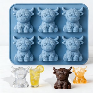 Puede incluir: Una bandeja de silicona azul para cubitos de hielo con seis formas de vaca de las Tierras Altas. Debajo, cubitos de hielo, una bebida con una rodaja de limón y dos figuras de vaca más en marrón y naranja. Un divertido accesorio de cocina.