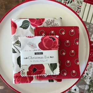 May include: A stack of Christmas-themed fabric squares on a white plate with a red rim. The fabrics feature red floral and wreath patterns on white and red backgrounds. The label reads "Christmas Eve".