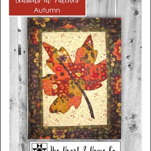 May include: A quilted wall hanging featuring a large autumn leaf design. The leaf is composed of various fabric patches in shades of orange, red, and yellow, with button accents. The text "Seasons in Patches Autumn" is displayed at the top.