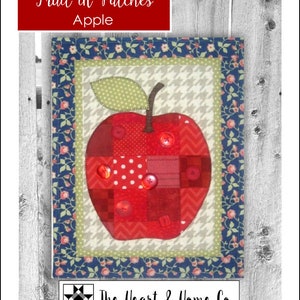 May include: A red patchwork apple quilt block with a green leaf and red buttons. The block is surrounded by a blue and white floral border. The title "Fruit in Patches Apple" is at the top of the image. The text "The Heart & Home Co." is at the bottom of the image.